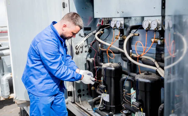 A professional specialist in blue overalls performing a high-precision maintenance check on a large industrial cooling system in Ajman.