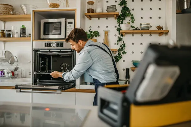 Close-up of a skilled engineer repairing a front-loading electric oven door during a oven repair services Ajman service call.