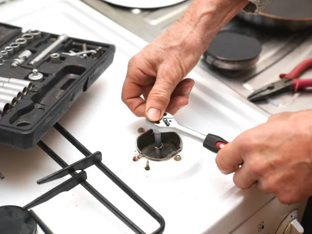 A repairman using professional tools for electric stove repair to fix a heating element on a home appliance.