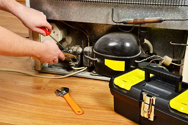 Close-up of a technician using a screwdriver and pliers to repair the compressor and internal components for refrigerator repair in Ajman.