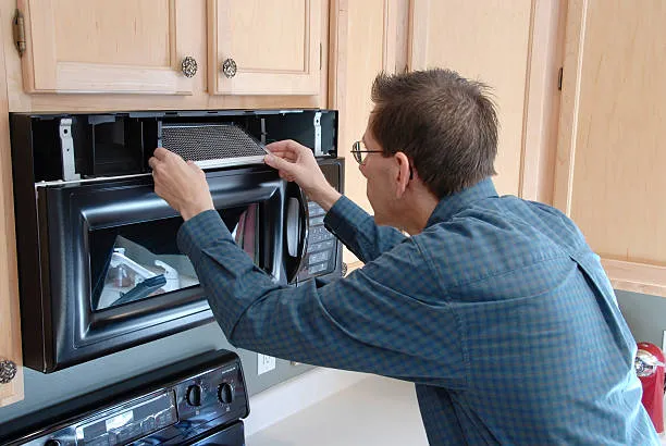 A skilled repairman inspecting the internal filter and components of a built-in microwave unit during a microwave oven repair abu dhabi visit.