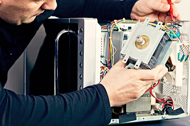 A senior technician in a gray uniform inspecting a built-in kitchen unit to provide expert microwave ovens sharjah repair services.
