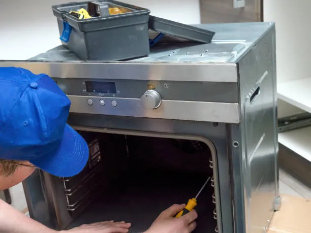 A professional technician inspecting the heating element of a built-in kitchen unit to provide expert oven repair services Ajman.