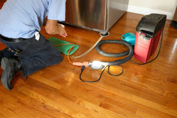 A close-up of professional refrigeration tools, including a manifold gauge set, vacuum pump, and safety helmet on a workbench.