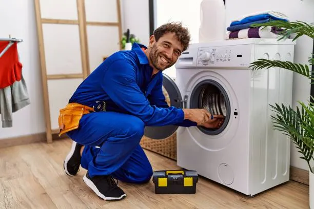 A smiling local specialist in a blue uniform performing a maintenance check for washing machine repair Ajman.