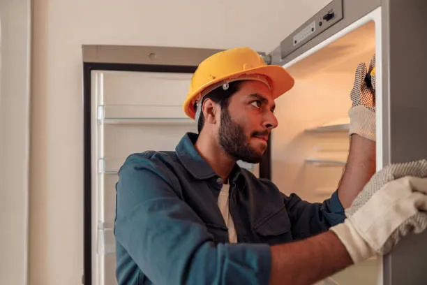 A professional technician wearing a hard hat and protective gloves repairing the internal thermostat of a residential unit in Dubai.