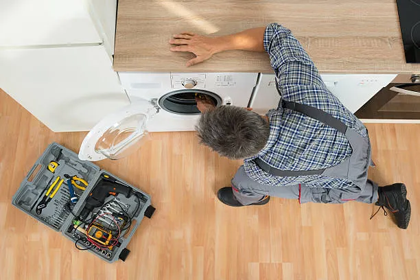 High angle view of a skilled repairman inspecting the drum of a front-load washer with a toolkit open on the floor for washing machine repair Dubai Marina.