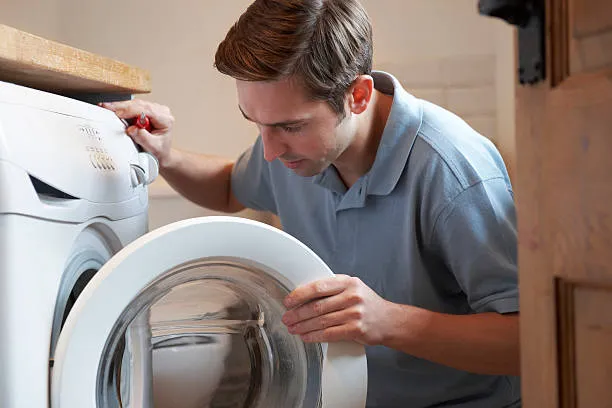 Close-up of a technician using a screwdriver to secure water inlet hoses on the rear of a washer for washing machine repair Sharjah.