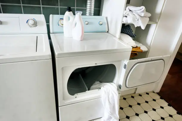 A white top-loading dryer in a laundry room with the door open, showing a white towel partially inside, representing common household appliance usage in the UAE.