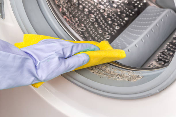 Close-up of woman is cleaning washer (washing machine) with a rag in rubber gloves.