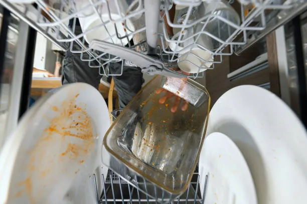 An interior view of dirty plates and glassware being loaded into a dishwasher, used to illustrate how proper loading saves water and energy for 24X7 Service UAE customers.